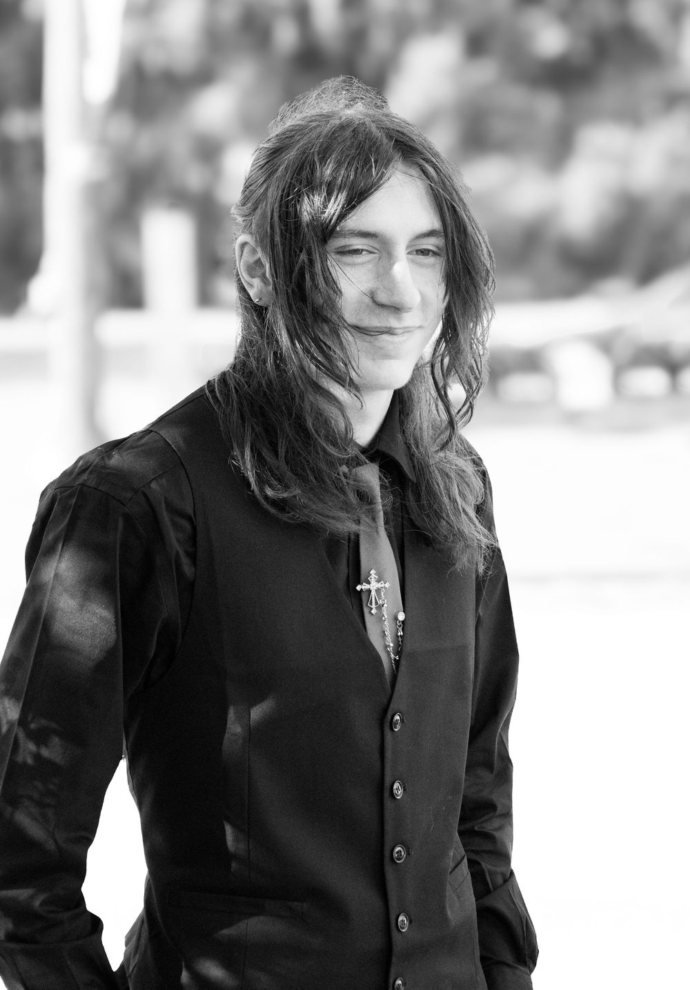 A black and white portrait of someone with long dark hair wearing a black buttoned shirt and smiling.