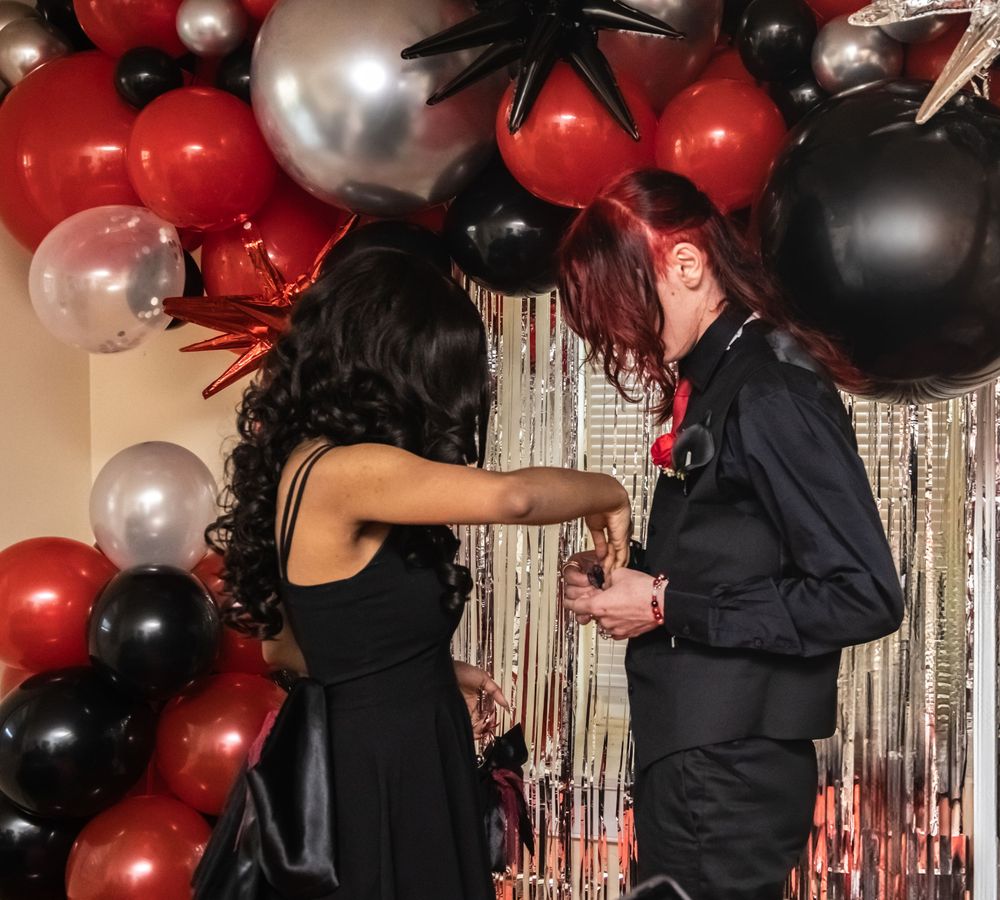 A festive party scene with black and red balloon arch decorations and silver tinsel curtain backdrop at a formal event.
