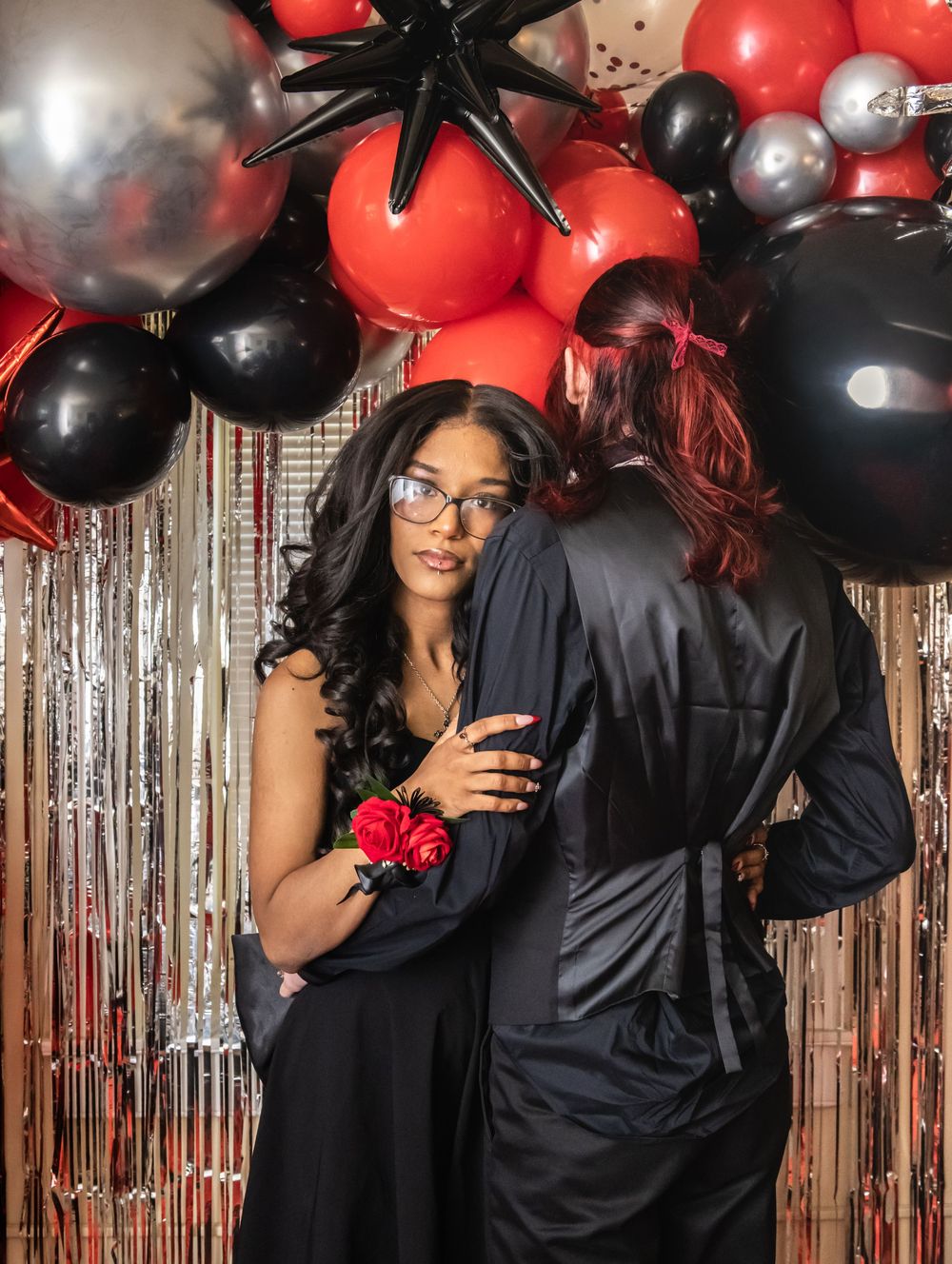 Festive prom photo with red and black balloons against a silver metallic backdrop at a formal dance event.