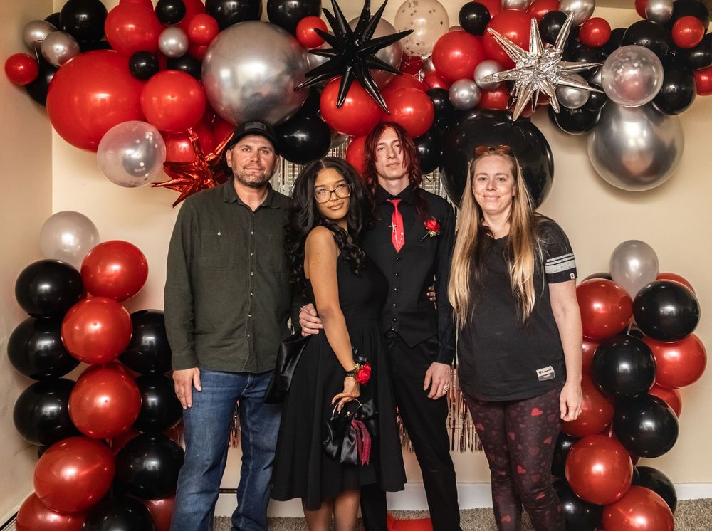 Group of people posing in front of festive red, black and silver balloon arch decorations.