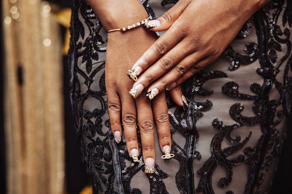 Hands with white manicured nails rest against a black lace and sheer evening dress.