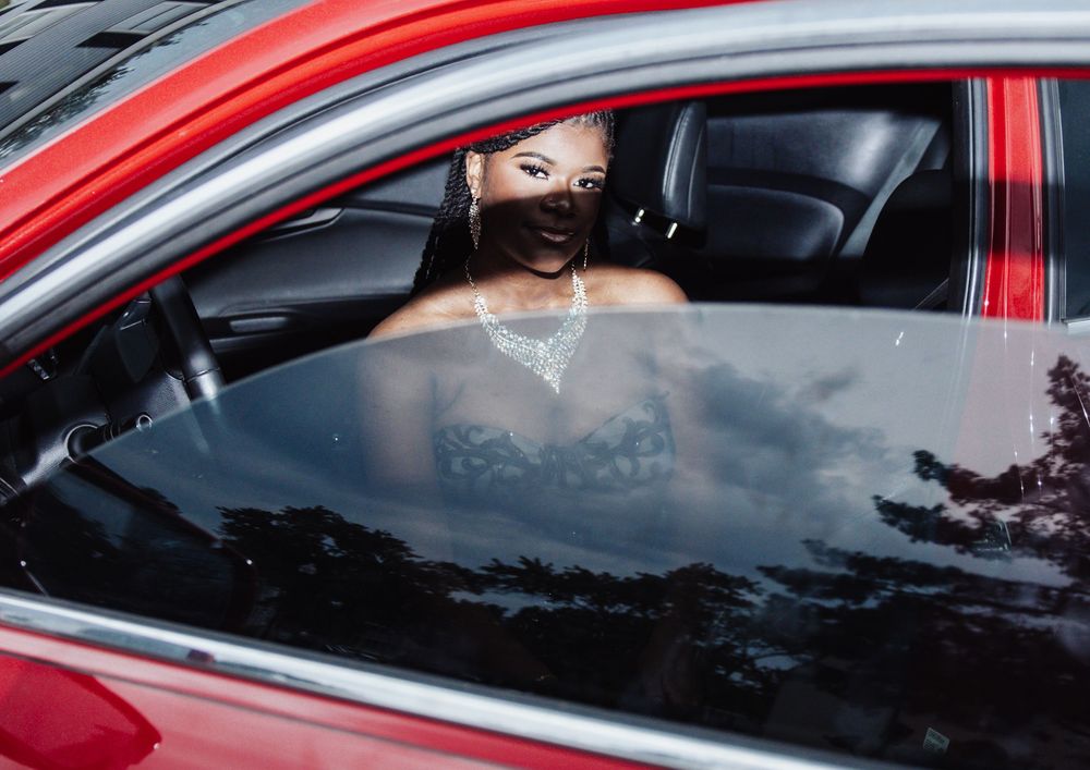 Red car interior view showing passenger wearing dark face mask and chains.