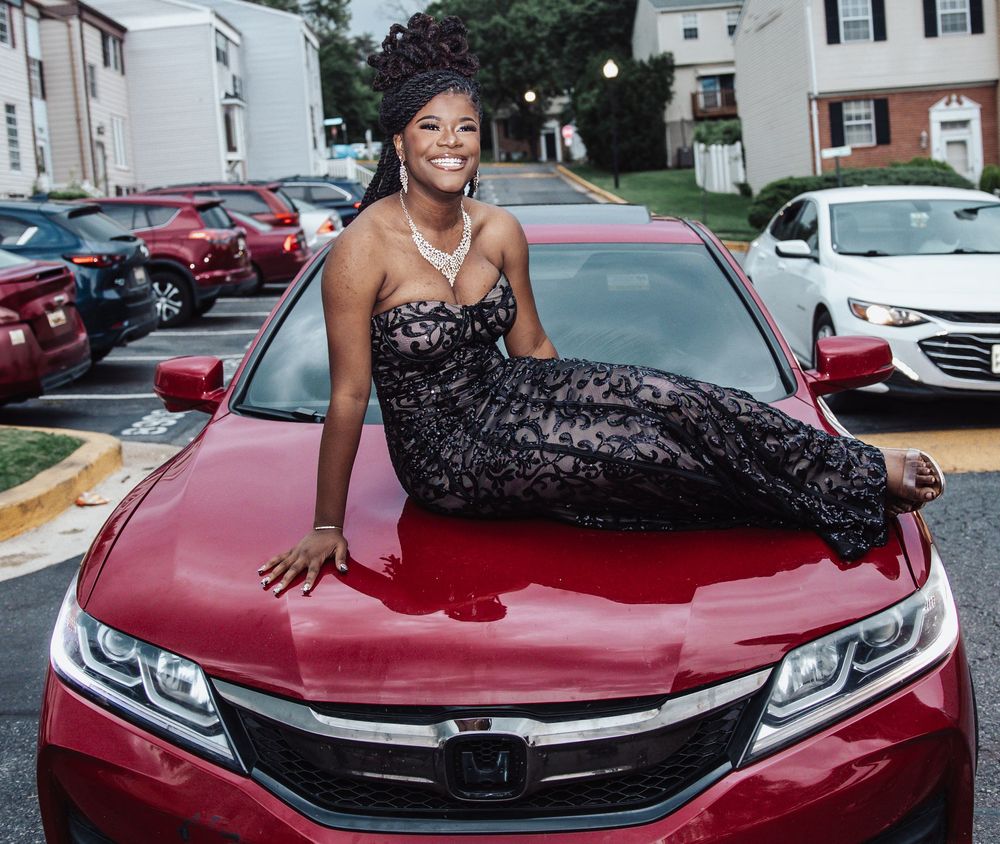 A formal sequined dress worn by someone posing on the hood of a red Honda Accord in a parking lot setting.
