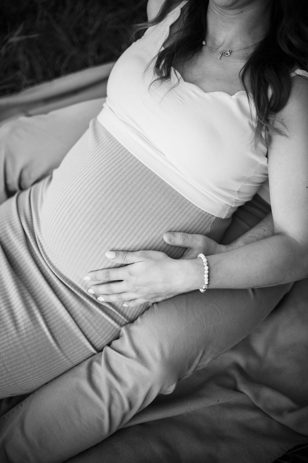 Ein schwarz-weißes Babybauchfoto, das Hände zeigt, die auf einem schwangeren Bauch in weißer, eng anliegender Kleidung ruhen.