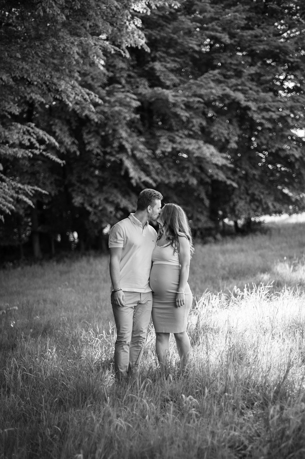 Ein romantisches Schwarz-Weiß-Foto eines Paares, das einen intimen Moment auf einer sonnenbeschienenen, von Bäumen umgebenen Wiese genießt.