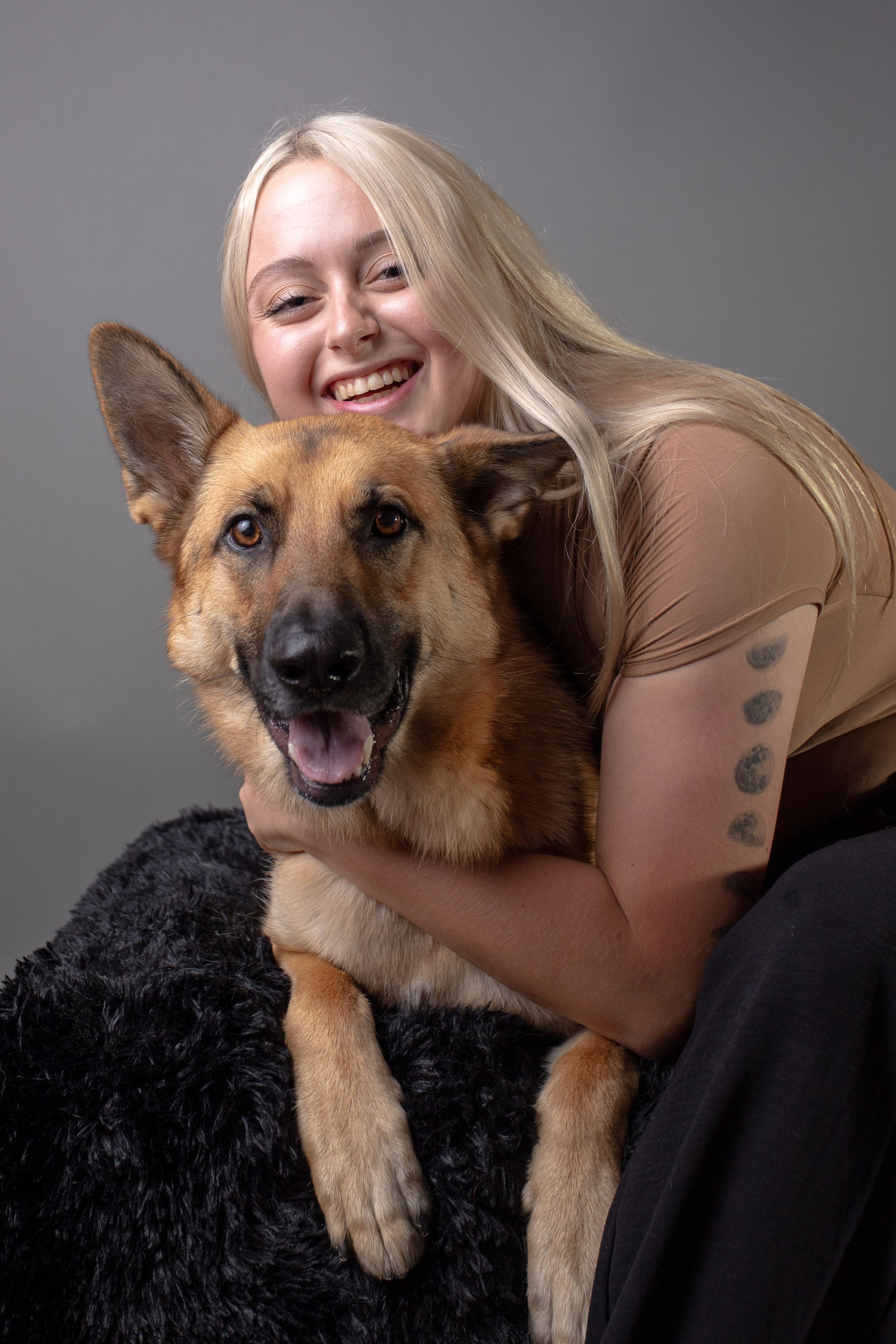 A happy German Shepherd mix dog with tan and black fur sits with their owner on a dark backdrop for a portrait.