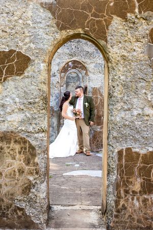 Rustic stone archway frames a romantic wedding moment against weathered stone walls at an historic venue.