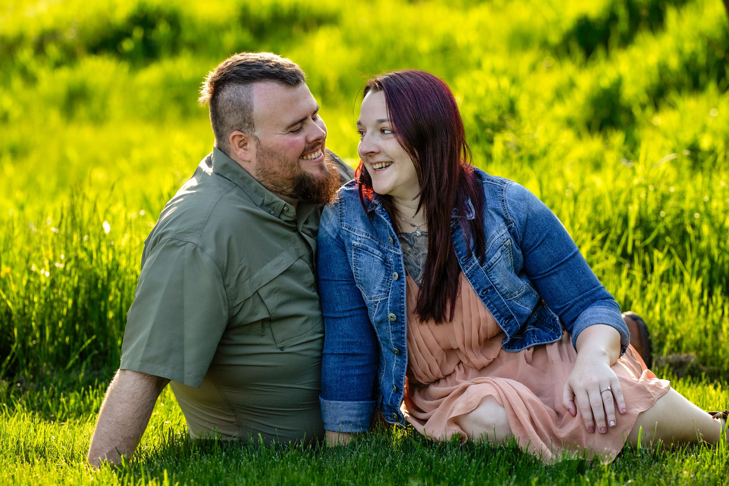 A couple sitting close together and laughing in a sunny meadow filled with vibrant yellow wildflowers.