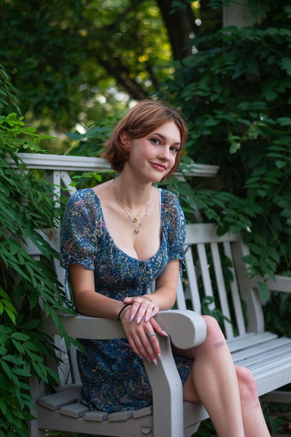 A portrait of a senior girl sitting on a bench with leaves and trees in the background