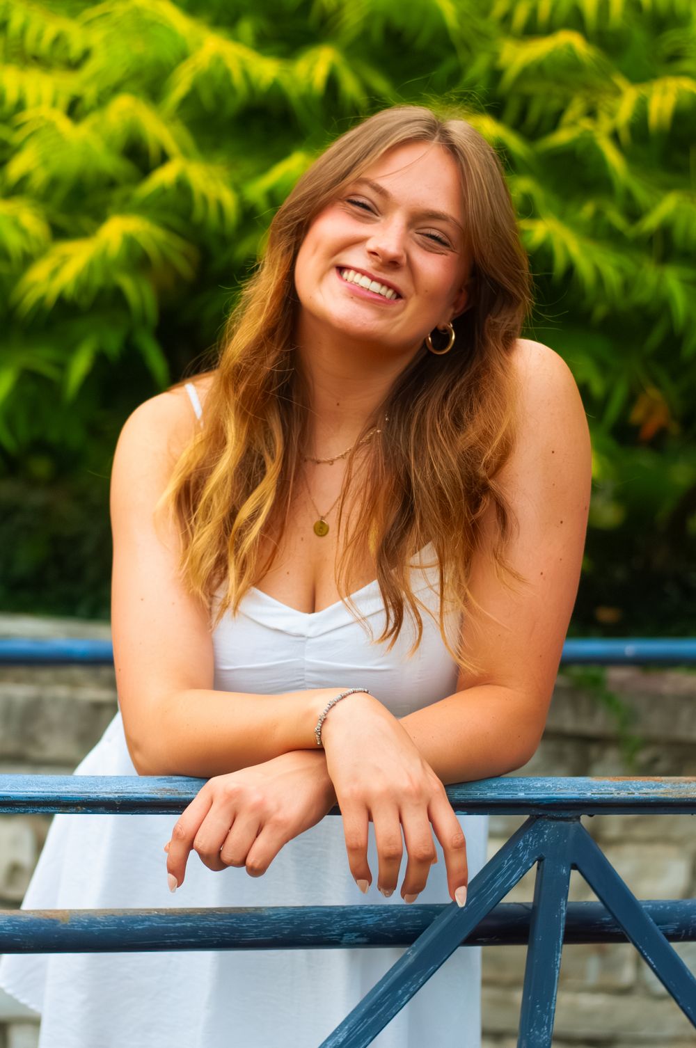 Portrait of a young woman leaning against a blue railing with trees in the background