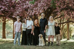 A group stands together outdoors under blooming pink cherry blossom trees with their dog during a spring photoshoot.