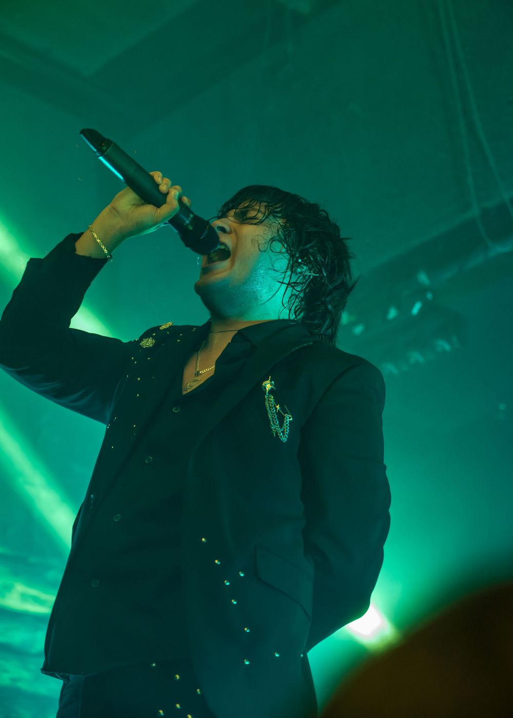 Rock vocalist singing passionately into microphone under vivid green stage lights during a live music performance.