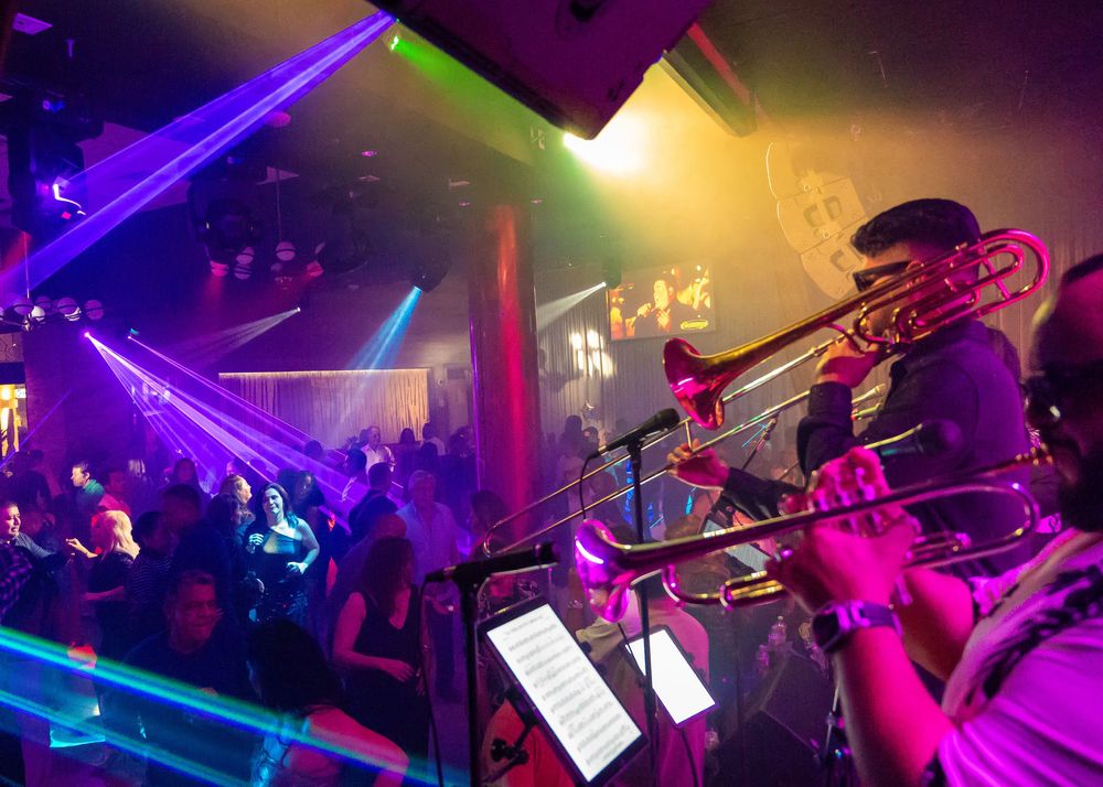 Trombone player performing on stage with colorful laser lights at a vibrant nightclub.