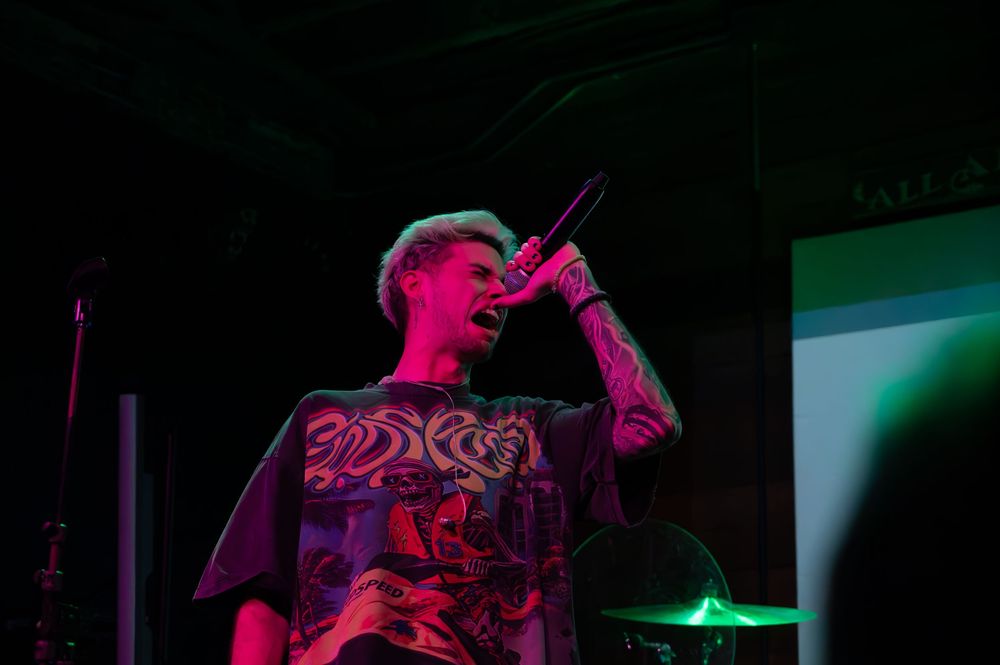 Tattooed artist performing on stage holding a microphone under vibrant pink stage lighting.