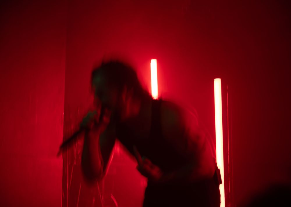 Silhouetted performer singing on stage surrounded by dramatic red lighting and neon light tubes.