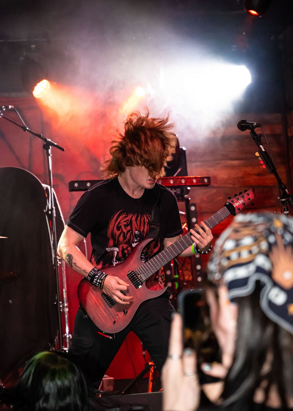 Metal guitarist shredding on red electric guitar under dramatic stage lighting at live concert.