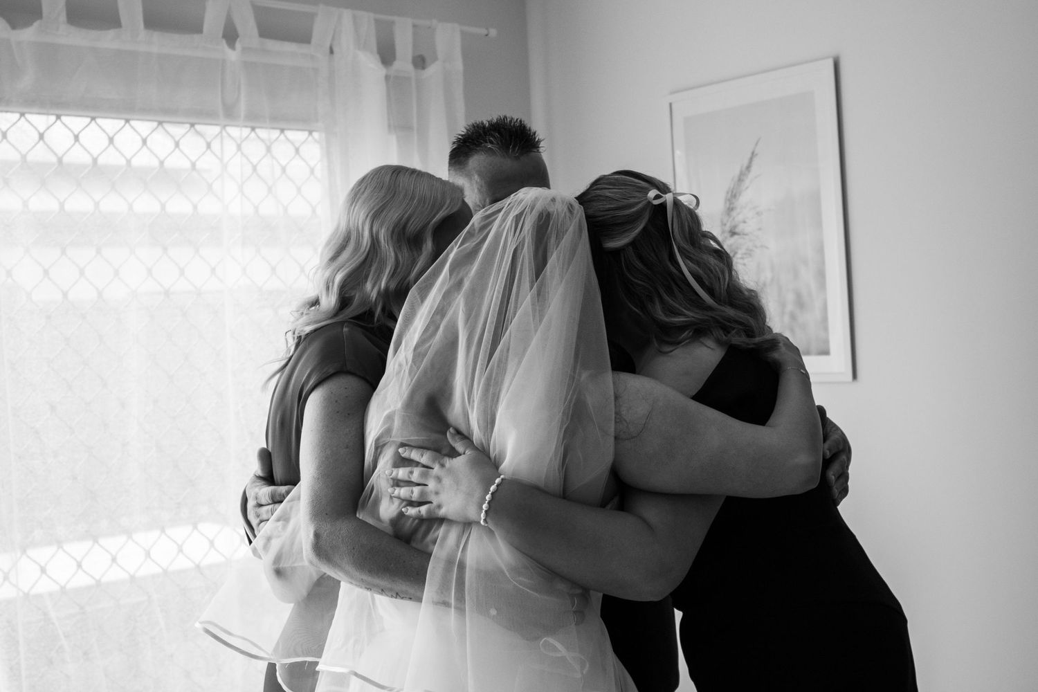 A black and white photo of a bride sharing a heartfelt group hug with family before the wedding ceremony.