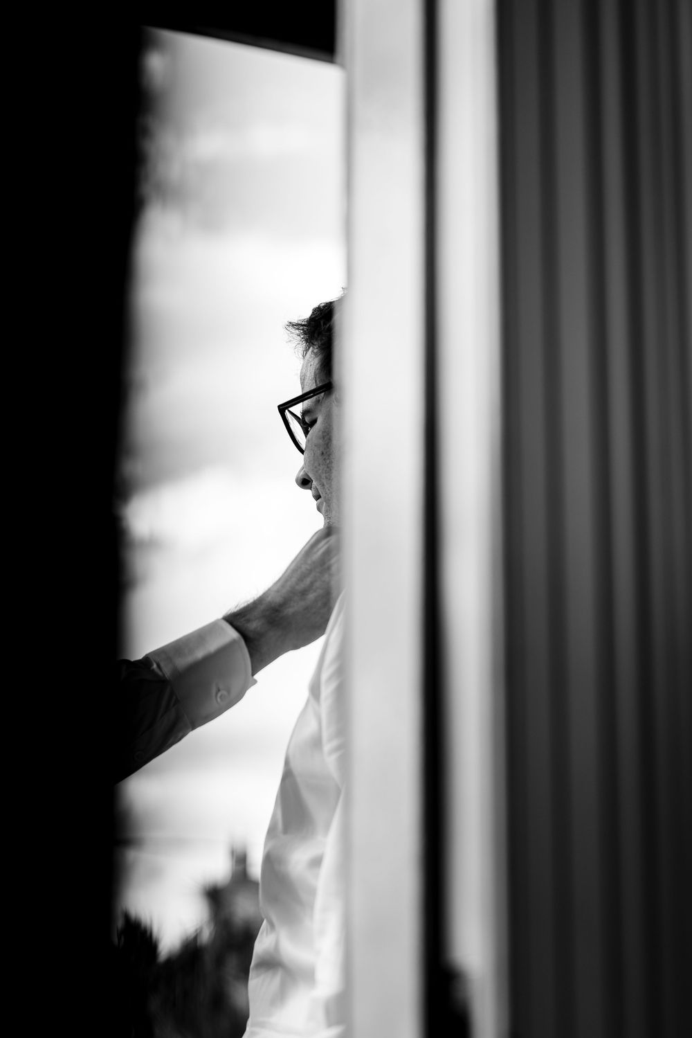 A black and white profile silhouette through window blinds shows someone wearing glasses in dramatic lighting.