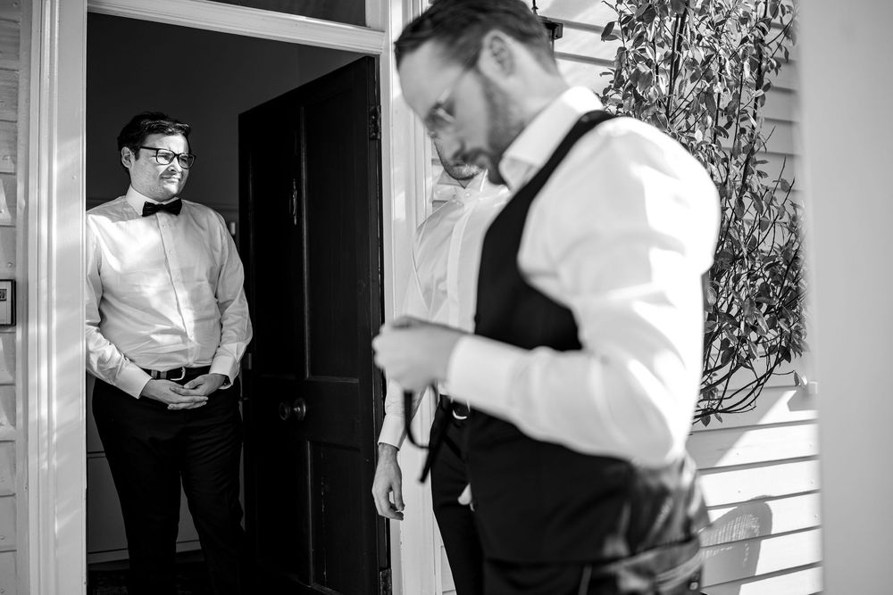 Black and white photo of men in formal attire getting ready in a room with natural light.