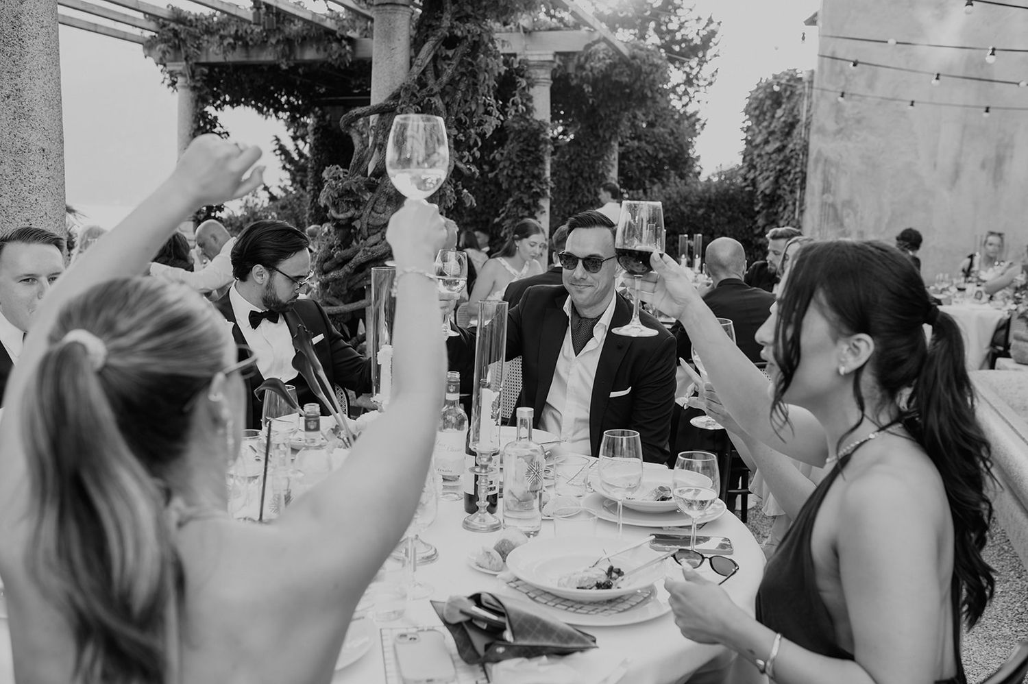 Wedding guests raise their glasses in a celebratory toast during an outdoor reception.