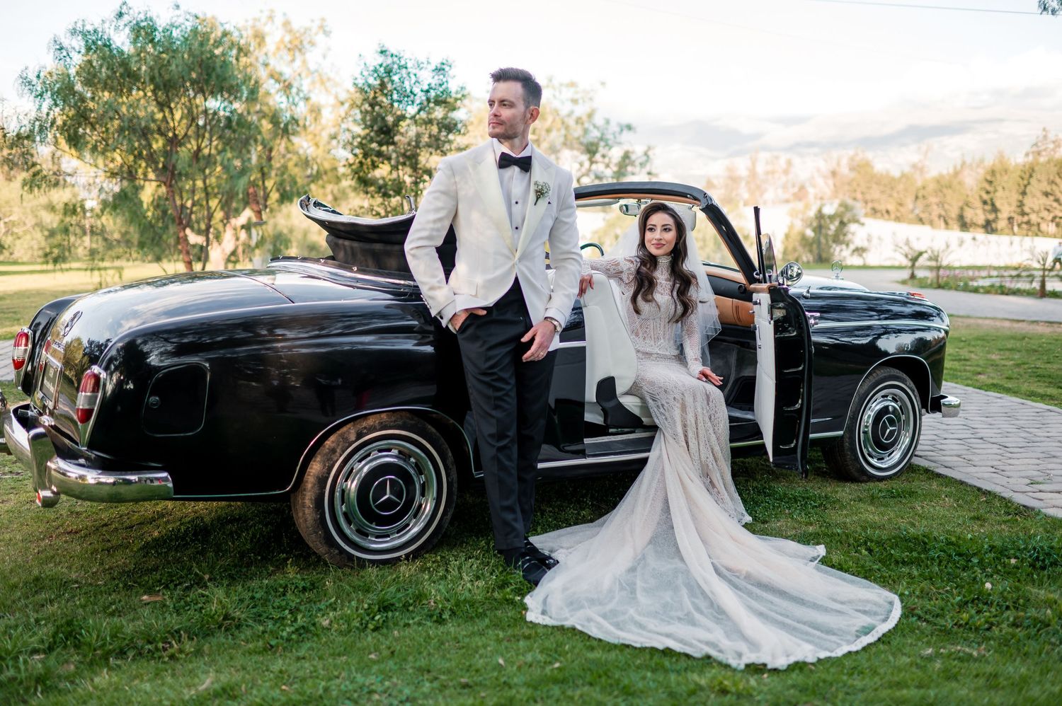 Elegant wedding photoshoot with vintage black Mercedes car in natural outdoor setting.