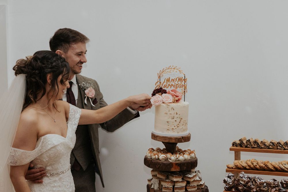A smiling bride and groom cut their elegant gold and floral wedding cake together.