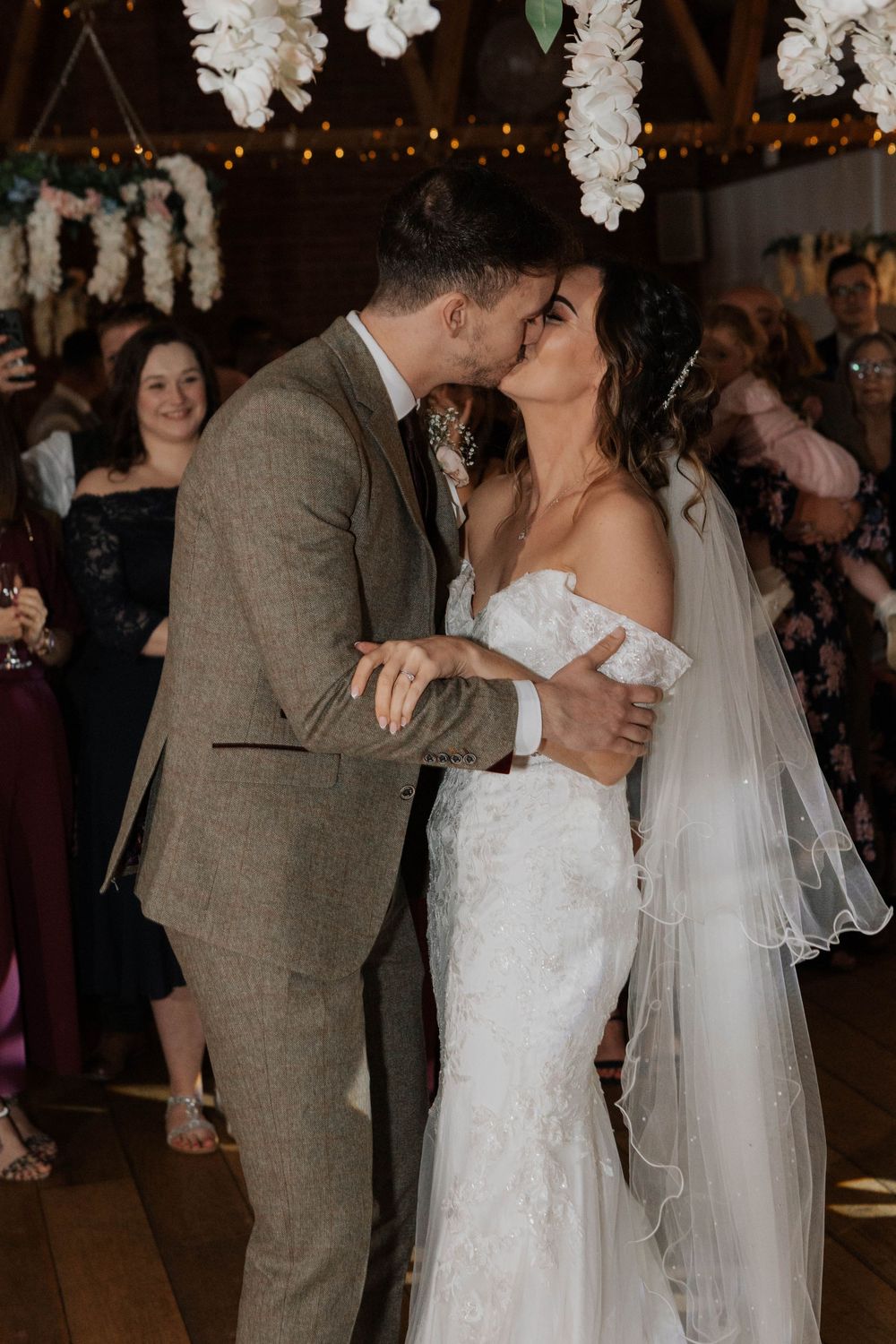 Bride and groom share a romantic first kiss at their wedding reception under floral decorations.
