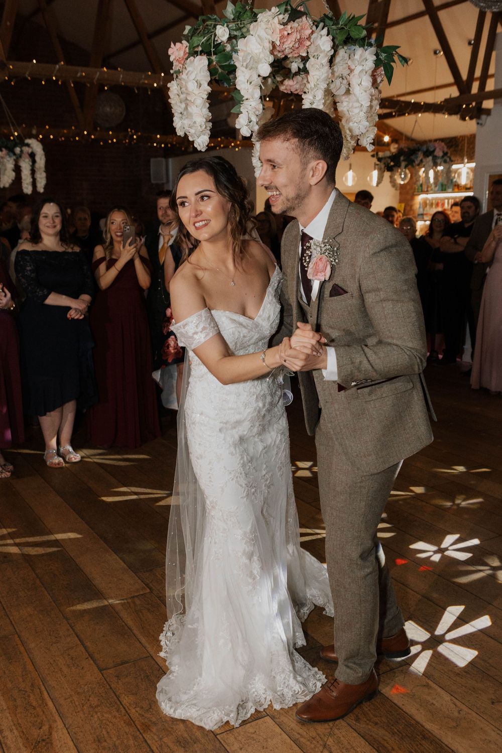 Smiling bride and groom enjoy their first dance together under hanging floral decorations at reception.