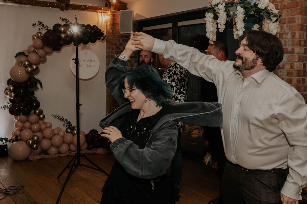 Wedding guests laugh and dance together under a balloon arch at a festive wedding reception.