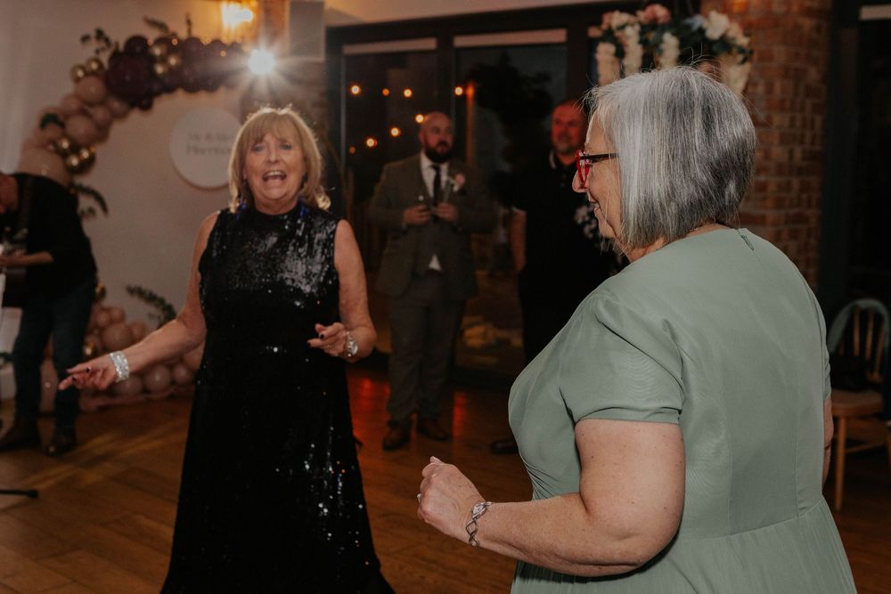 Two women dance and celebrate joyfully on the wedding reception dance floor.