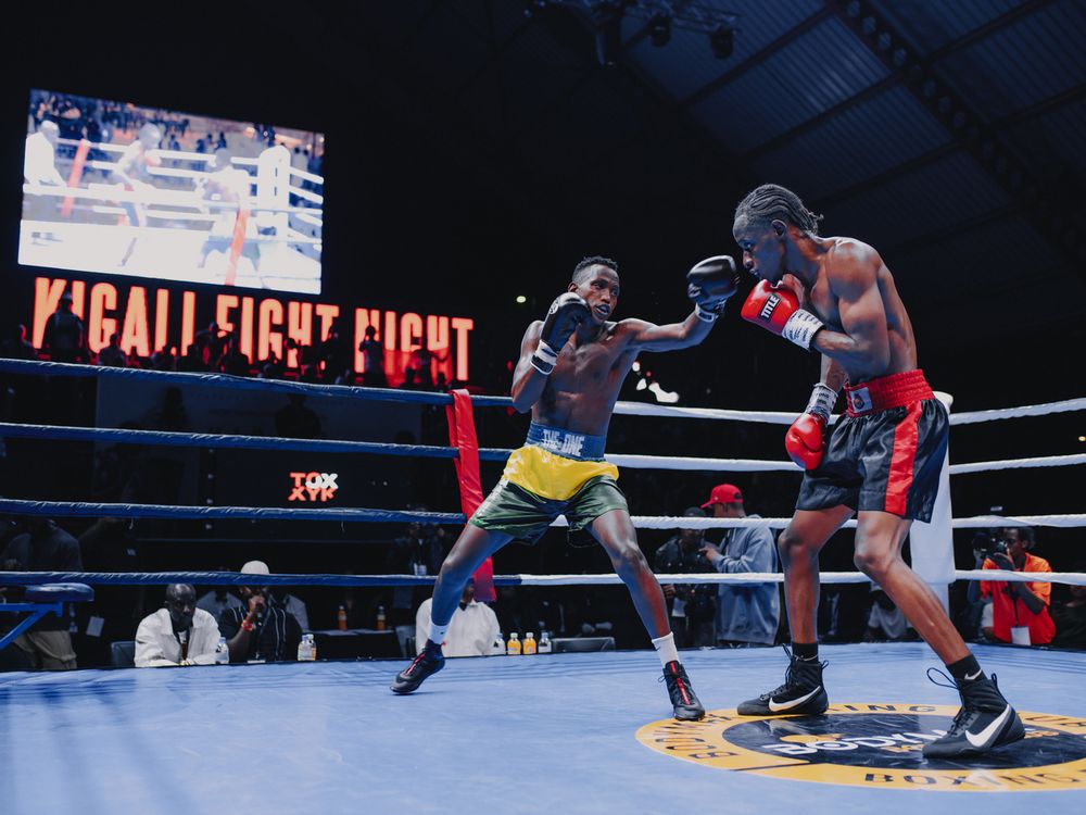 Two boxers exchange punches during a professional boxing match in a ring with bright lights overhead.