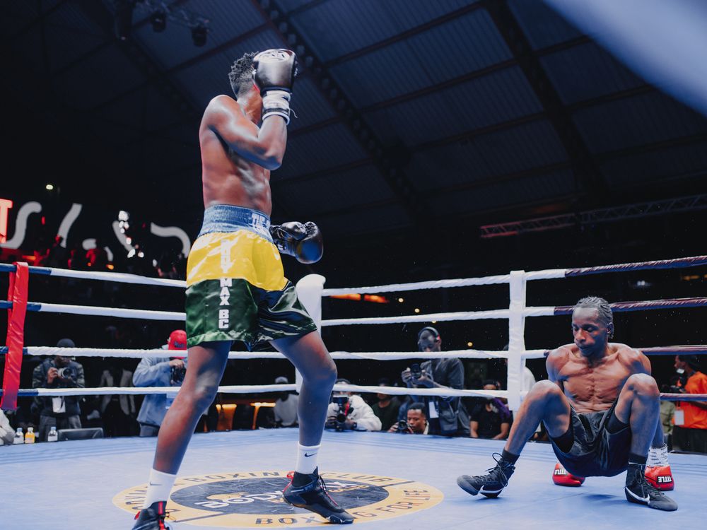 Two boxers in a professional boxing ring square off during an intense match with spectators watching in the background.