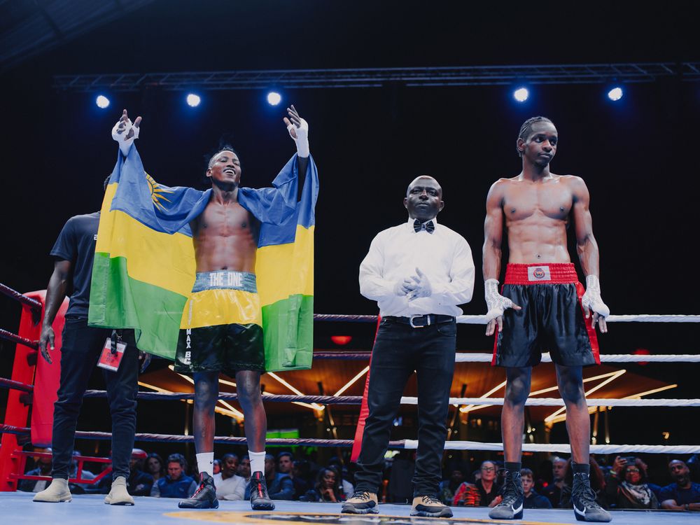 Boxers celebrate in the ring after a match with flags and raised arms under blue spotlights.