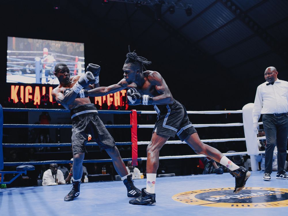 Two boxers exchange punches during an intense fight night match in a dimly lit boxing ring.