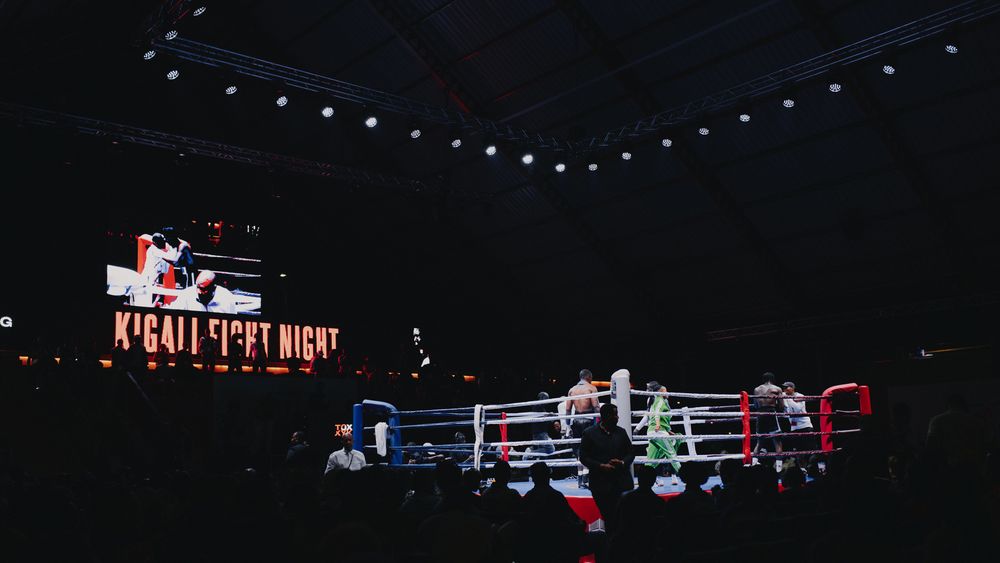 Two boxers exchange punches in a dimly lit boxing ring during an intense match.