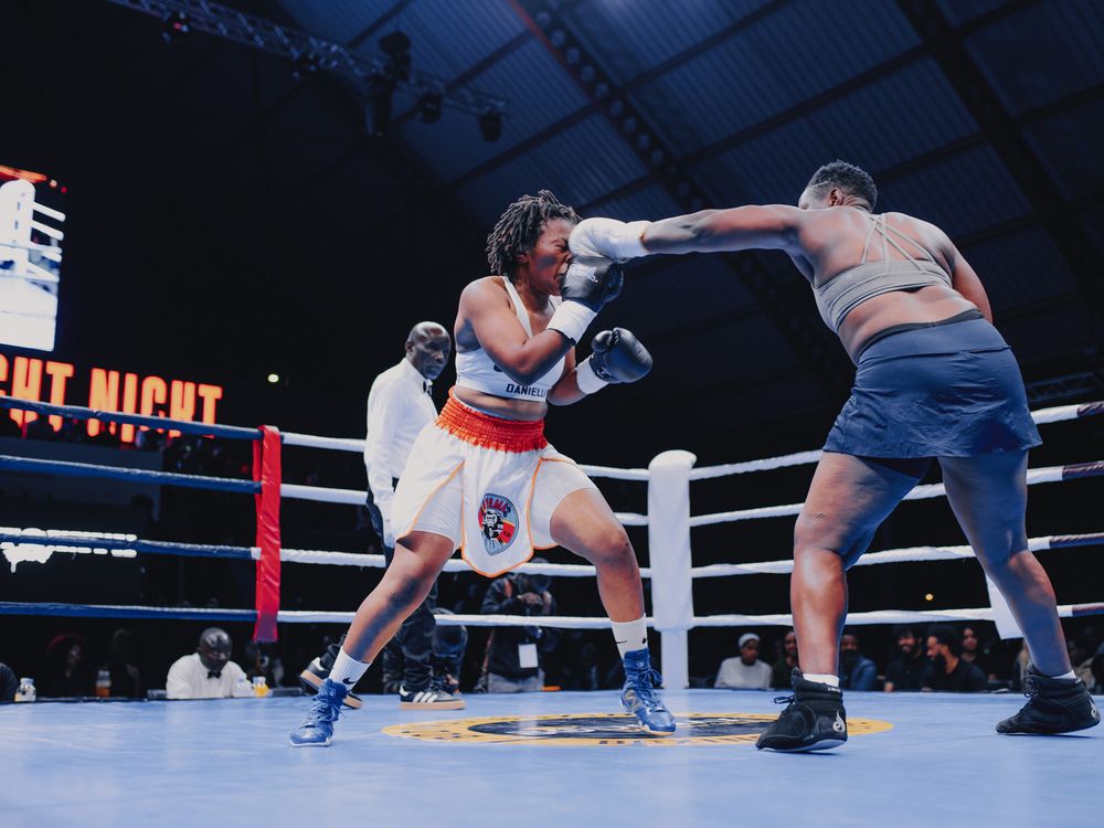 Two boxers exchange punches during an intense match in a professional boxing ring under bright lights.