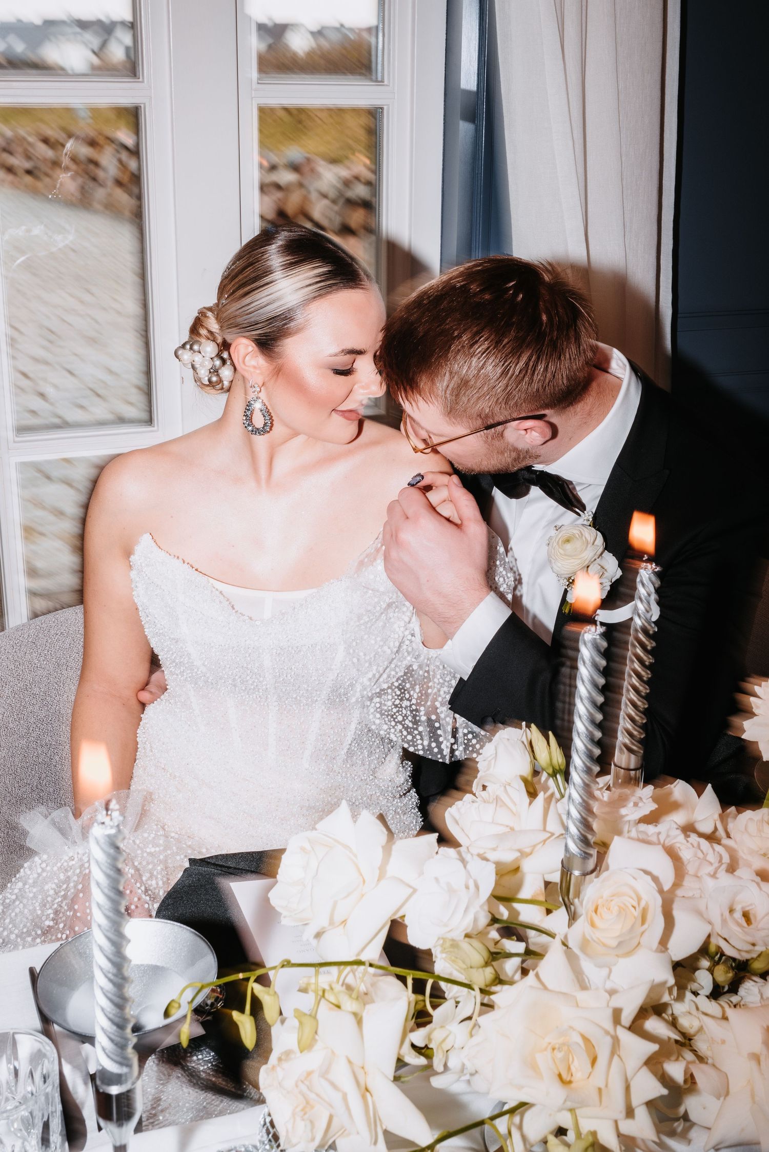 Elegant wedding couple sharing intimate moment at reception table decorated with white roses.