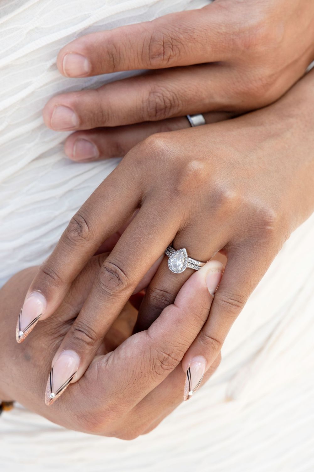 Elegant hands with French tip manicure display a sparkling diamond engagement ring against white fabric.