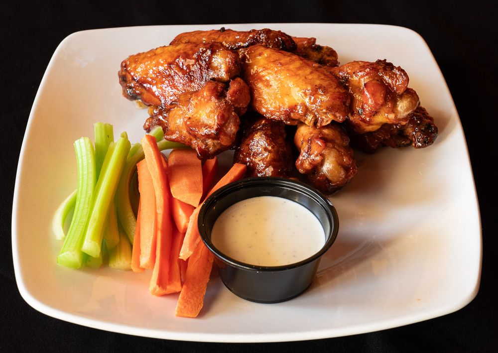 A plate of buffalo chicken wings served with celery sticks, carrots, and creamy dipping sauce.