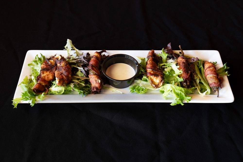 Bacon wrapped scallops served on a white rectangular plate with fresh lettuce and dipping sauce.