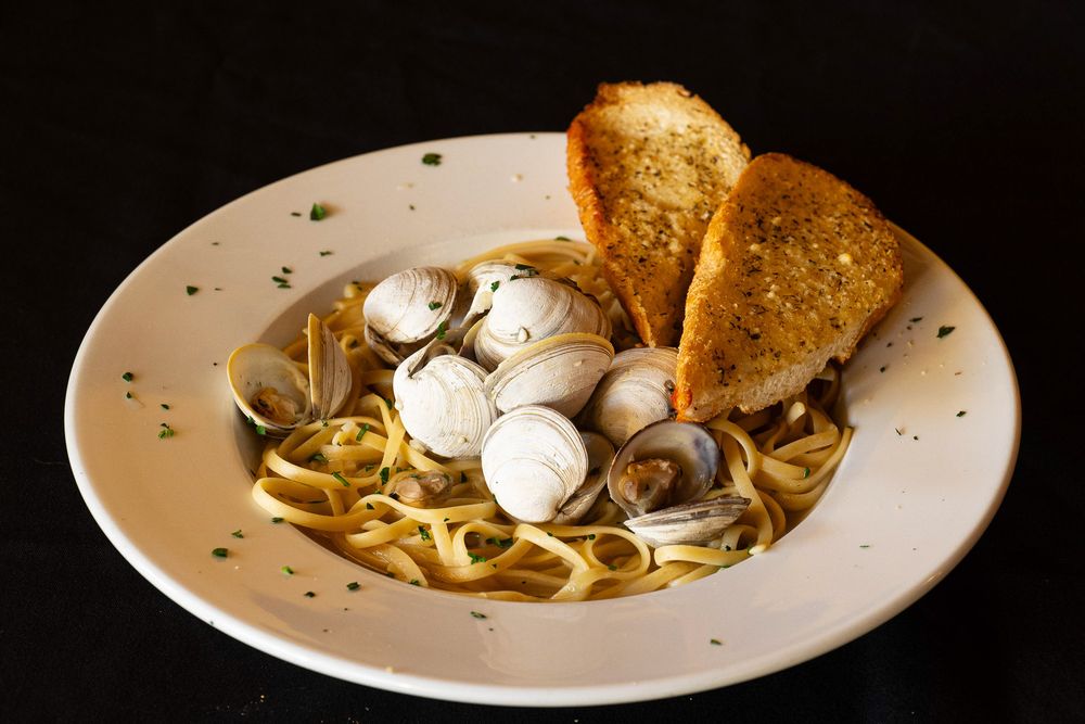A bowl of steaming pasta with clams in white wine sauce garnished with fresh herbs and black pepper.