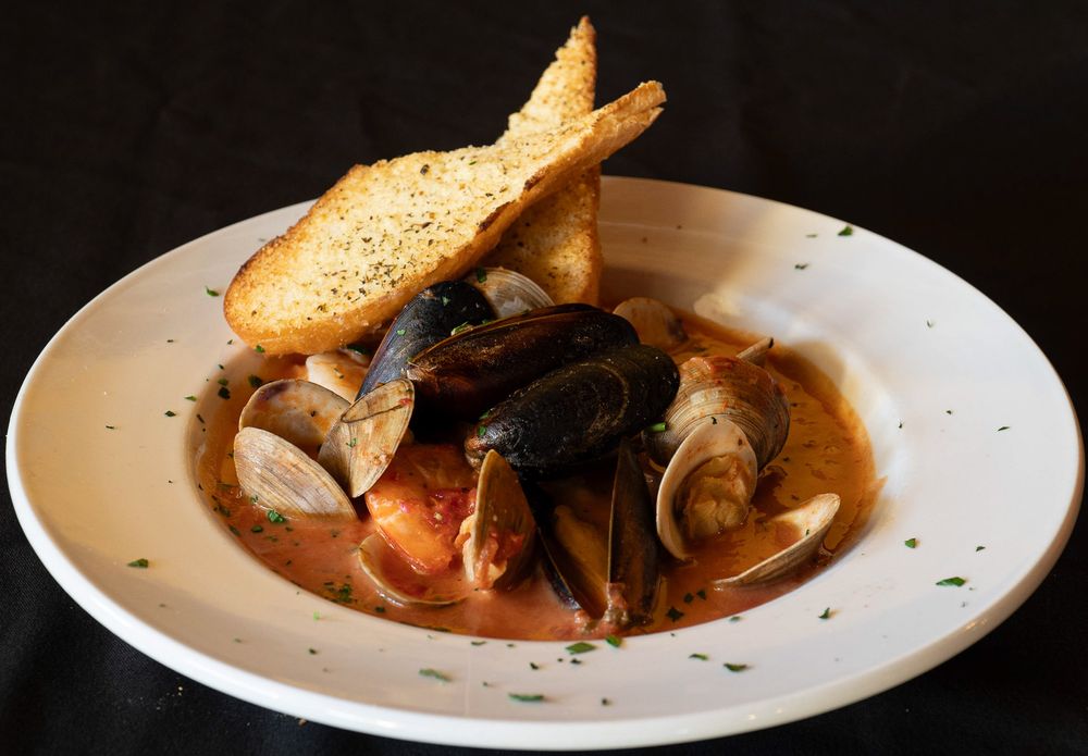 A bowl of steaming seafood soup with mussels, clams, and toasted bread served in a white ceramic dish.