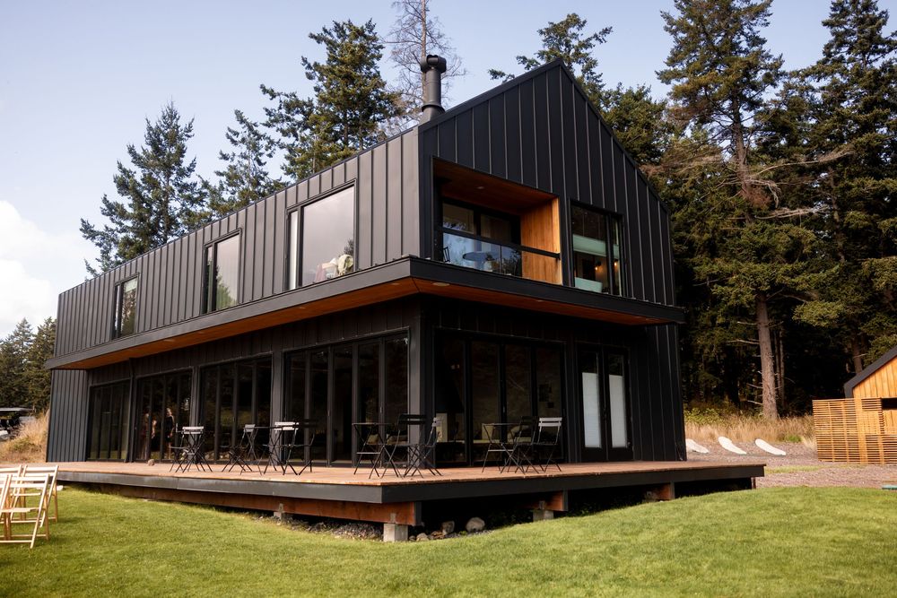 Modern black architectural building with wood accents nestled among pine trees.