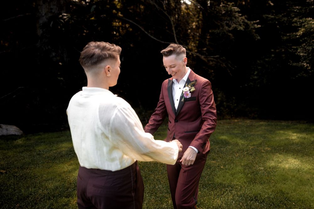 Two people in formal attire stand together on a grassy lawn during what appears to be a wedding celebration.