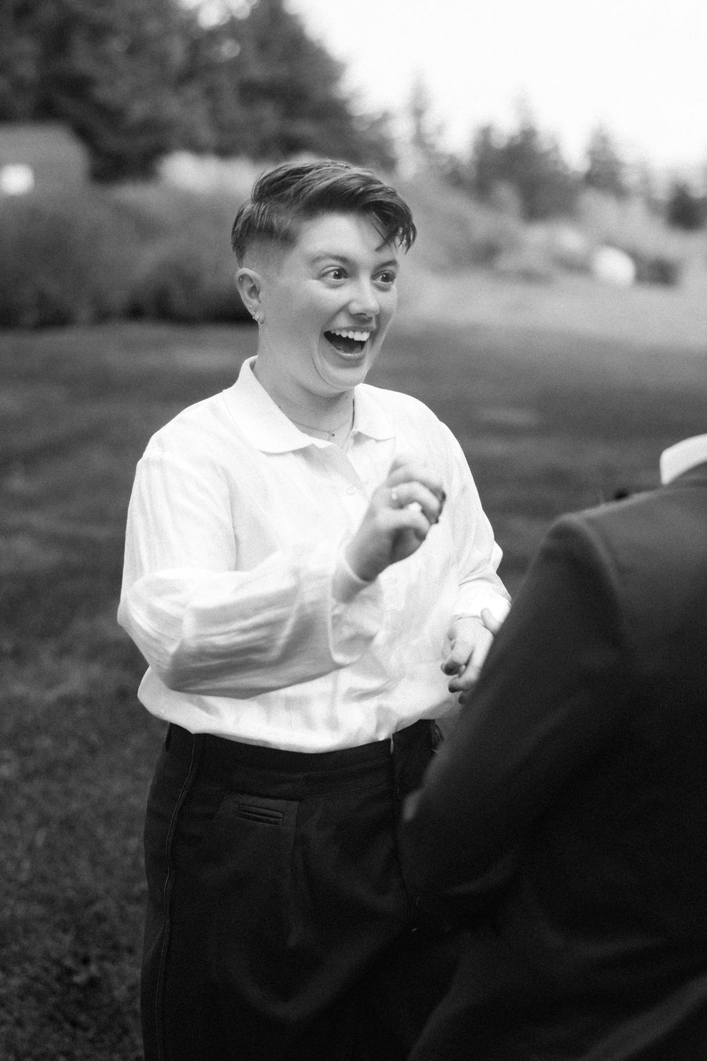 Black and white photo captures joyful laughter during outdoor wedding celebration.