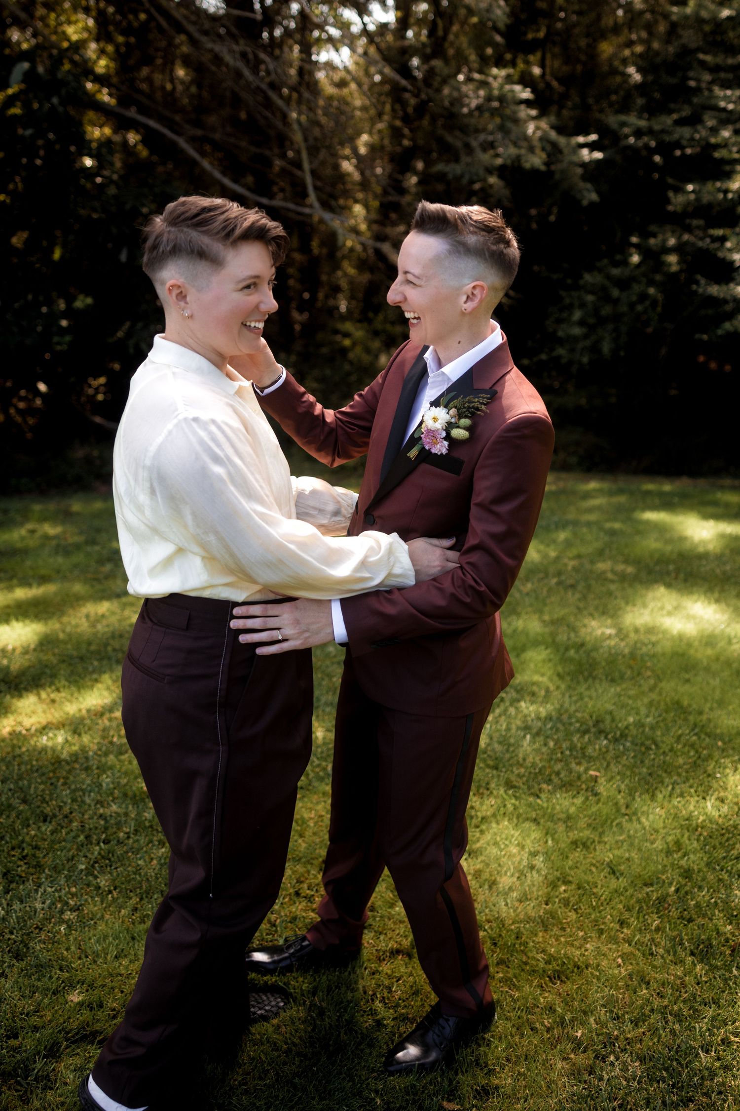 Two people in formal attire sharing playful moments on sunny grass.