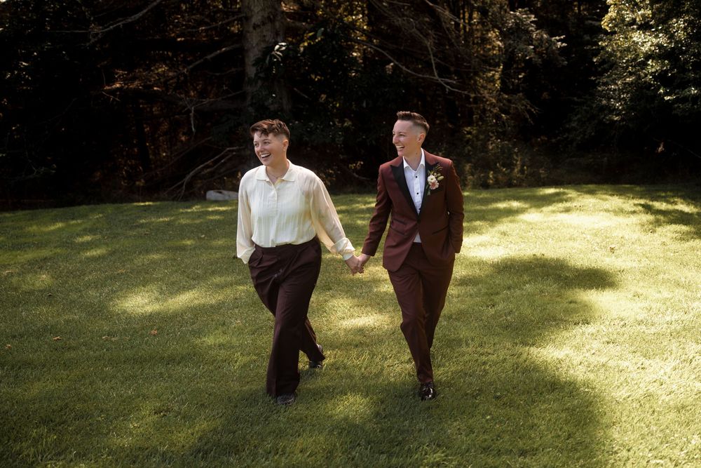 Two people walking together on a sunlit grassy lawn wearing coordinated formal attire.