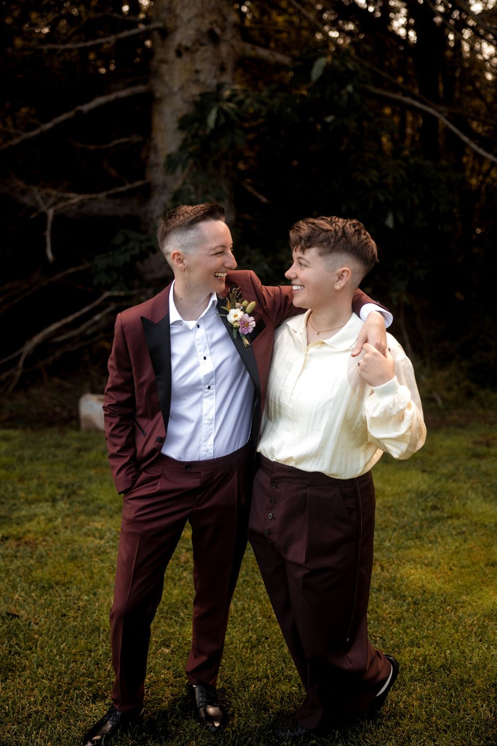 A couple sharing a joyful moment together outdoors while wearing burgundy and cream formal attire.