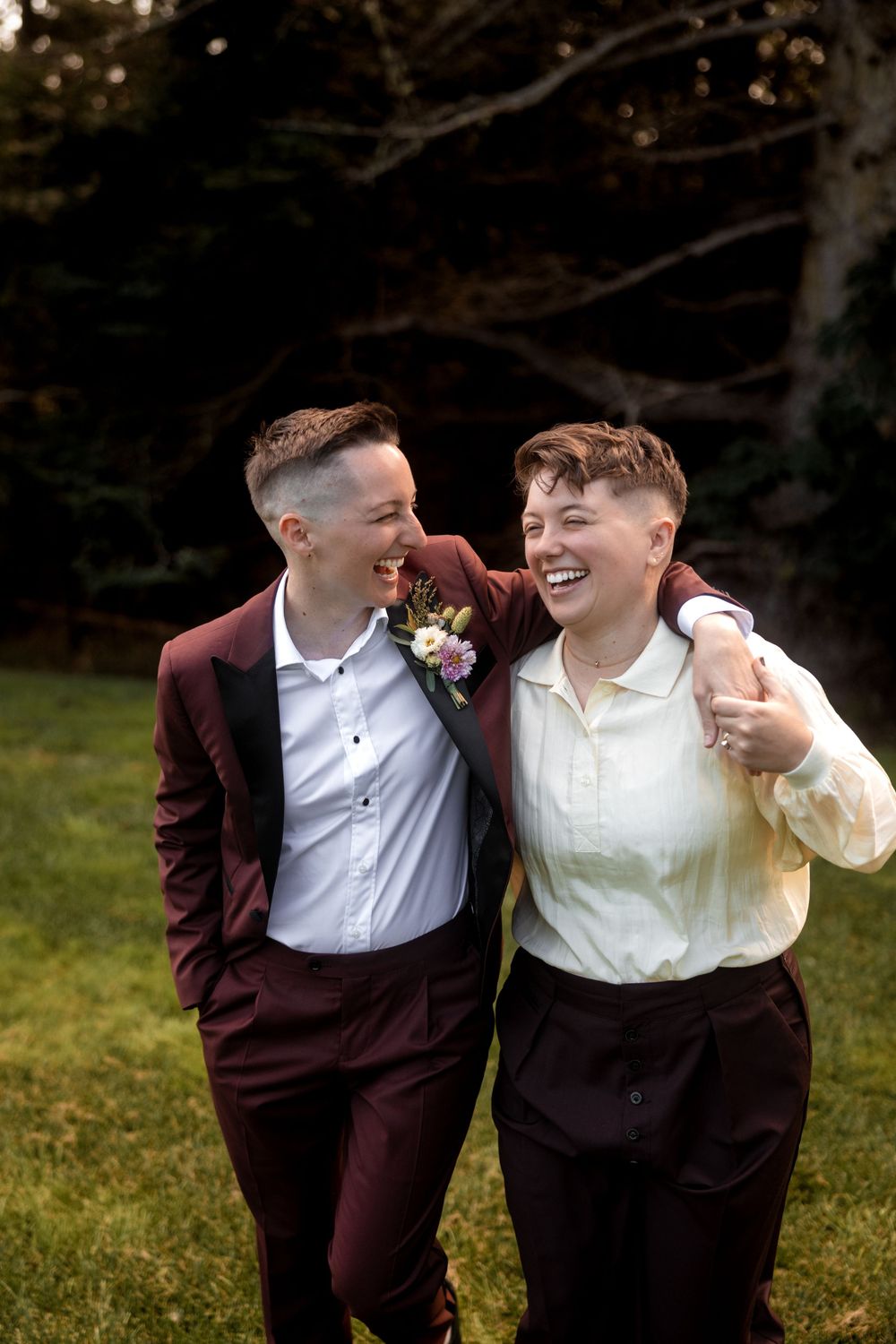 Two people in burgundy and white formal attire share a joyful moment together outdoors.