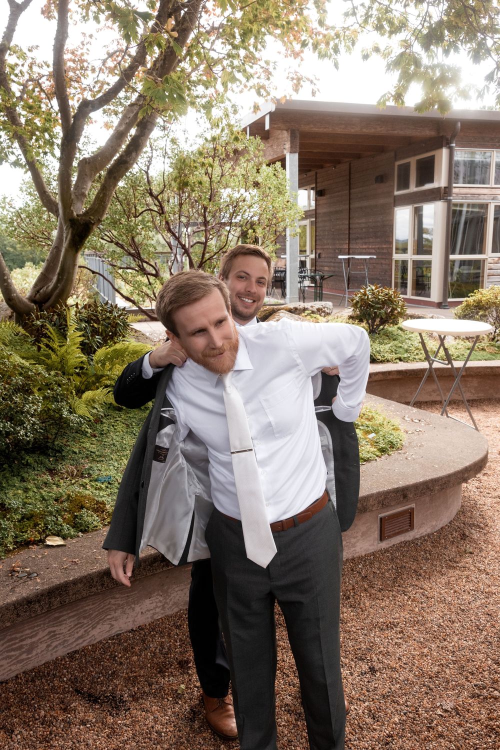 Groomsmen sharing playful moments and laughter outside a modern building.